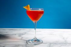 a red drink in a wine glass with an orange slice on the rim sitting on a marble counter