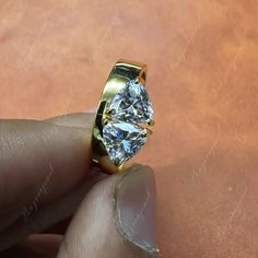 a person holding a gold ring with a large diamond in it's middle finger