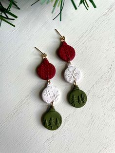 three different earrings hanging from a christmas tree ornament on a white table with pine branches