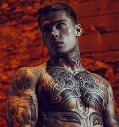 a man with tattoos standing in front of a brick wall and looking at the camera