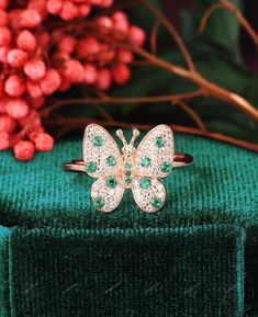 a butterfly ring with green and white stones sits on top of a green velvet box