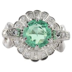 An approximately 2.00-carat natural light green round-shaped emerald measuring 8 x 6.12 mm is the centerpiece of this dazzling vintage band surrounded by a halo of fifteen single cut diamonds totaling approximately 0.15 carats atop an openwork scrolling gallery. Additional diamonds adorn the shoulders and attach to a split shank fashioned in 10kt white gold. Green Emerald Ring With Halo Round Cut, Green Diamond Halo Ring In Round Cut, Art Deco Emerald Ring With Rose Cut Diamonds, Art Deco Green Emerald Ring With Rose Cut Diamonds, Green Emerald Ring With Rose Cut Diamonds, Vintage Green Diamond Ring In Platinum, Vintage Green Diamond Platinum Ring, Vintage Green Diamond Ring With Center Stone, Vintage Green Emerald Ring With Brilliant Cut