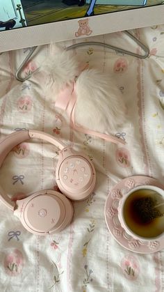 a white dog laying on top of a bed next to headphones and a cup of tea