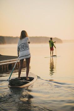 two people are paddling on surfboards in the water at sunset, one is holding a paddle