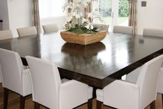 a dining room table with white chairs and flowers in a basket on the centerpiece