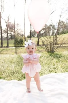 a baby girl standing in the grass with a balloon