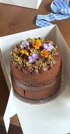 a chocolate cake in a box with flowers on top, ready to be cut and served