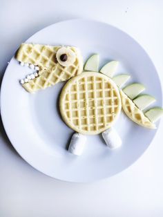 a white plate topped with waffles and fruit shaped like a crocodile head on top of each other