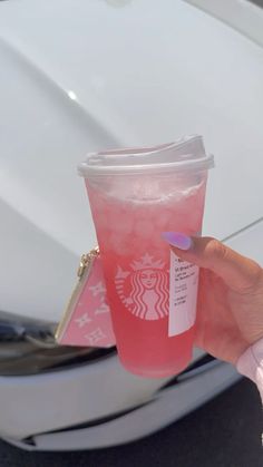 a person holding up a pink drink in front of a white car