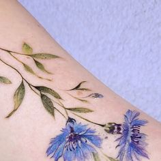 a tattoo with blue flowers and green leaves on the back of a woman's arm