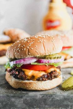 a cheeseburger with pickles, onions and tomato on a table next to some ketchup