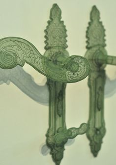 an intricately designed green glass candle holder on a white wall with two candles in the middle