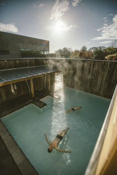 two people swimming in a pool with steam coming out of the water and sun shining down on them