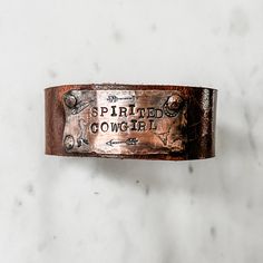 Spirited Cowgirl bracelet is a handmade beauty any free spirited boho cowgirl will boldly and proudly wear. This showpiece has a gorgeous medallion featuring stamped cowgirl symbols including arrows, horse, feather and steer head as well as hand stamped lettering. Handmade in Idaho by Weathered Soul exclusively for Bourbon Cowgirl. Limited Edition, high quality jewelry that is as unique and authentic as you! Due to their handcrafted nature, slight variations will occur. The feel and design of th Rustic Brown Bracelet With Concho, Rustic Brown Concho Bracelets, Adjustable Rustic Bracelet In Distressed Brown, Rustic Stamped Adjustable Cuff Bracelet, Rustic Adjustable Stamped Cuff Bracelet, Rustic Adjustable Bracelet In Distressed Brown, Rustic Stamped Leather Bracelet, Adjustable Stamped Bracelets, Rustic Adjustable Distressed Brown Bracelet