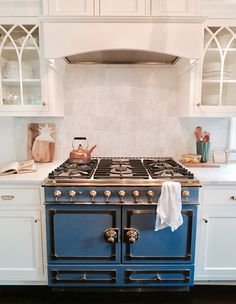 a blue stove top oven sitting inside of a kitchen next to white counter tops and cabinets