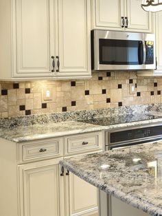 a kitchen with white cabinets and granite counter tops, stainless steel microwave above the stove