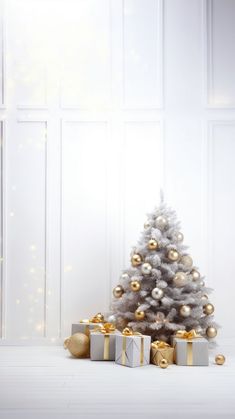 a white christmas tree with gold and silver presents under it in front of a window