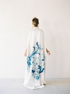 Guo Cape | Silk Embroidered Cheongsam Cape Luxury meets comfort. Made from a silky smooth fabric, this floor-skimming cape brings an ethereal dimension to a sleek underlayer with its draping silhouette. Combining elements of tradition such as the mandarin collar, pankou knot, and a beautifully embroidered blue dragon and phoenix motif, this cape is made to bring out your inner queen. ✨Check out our additional dresses at www.eastmeetsdress.com✨ The Details: * White silk fabric * Blue dragon and p Elegant Embroidered Silk Kimono, Silk Kimono With Floral Embroidery, Long Fitted Kimono For Wedding, Blue Silk Kimono For Wedding, Blue Silk Wedding Kimono, Long Embroidered Kimono For Wedding, Wedding Embroidered Kimono With Kimono Sleeves, Long Floral Embroidered Kimono For Wedding, Embroidered Wedding Kimono