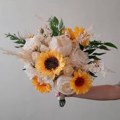 a person holding a bouquet of sunflowers and other flowers in their hand on a white background