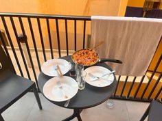 a small table with plates and silverware on it, next to a towel hanging from the balcony