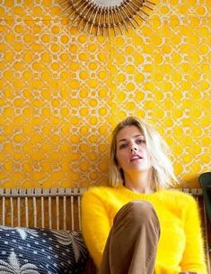 a woman sitting on top of a couch next to a yellow wallpapered wall