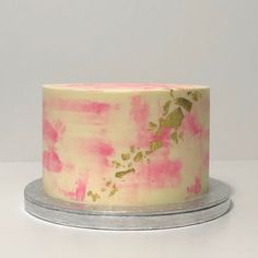 a cake with pink and gold frosting on a silver platter next to a white wall