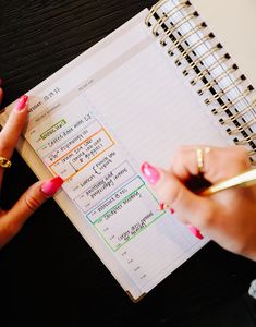 a woman's hands holding a pen and writing on a planner