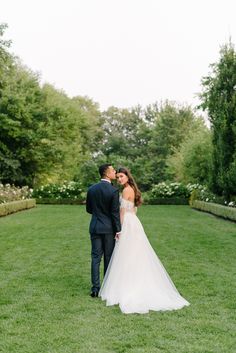 a bride and groom standing in the grass at their wedding day, looking into each other's eyes