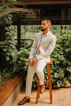 a man sitting on top of a wooden chair in front of some plants and trees