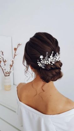 a woman wearing a bridal hair comb with flowers on it's head, in front of a white wall