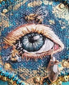 an eye is shown in the middle of a piece of fabric with gold and blue beads