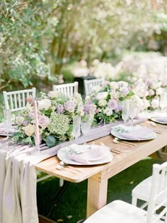 an outdoor table set with white and pink flowers, greenery and candlesticks