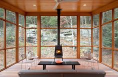 a living room filled with furniture and a fire place in front of large windows that look out onto the woods