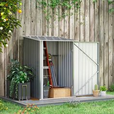 an outdoor storage shed is shown with plants and boxes in the foreground, next to a wooden fence