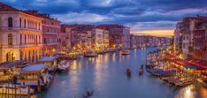 boats are parked on the water in front of buildings and lights at dusk, along with dark clouds