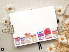 an open notebook with four jars of jams on it and daisies in the background