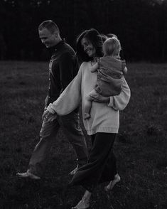 a man and woman walking through a field with a child on their back, in black and white