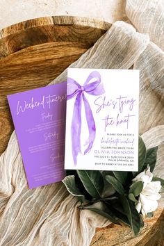 a purple and white wedding card with a bow on it next to a bouquet of flowers