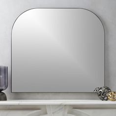 a mirror sitting on top of a white mantle next to a vase and candle holder