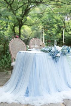 a blue table cloth with flowers and candles on it in front of an outdoor setting