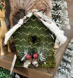 a green birdhouse sitting on top of a wooden shelf next to christmas tree ornaments