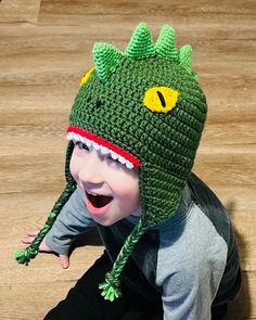 a child wearing a crocheted hat with a green dragon on it's face