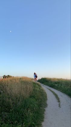 two people are walking down a path in the grass and one person is flying a kite