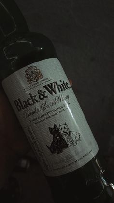 a bottle of black and white wine in someone's hand