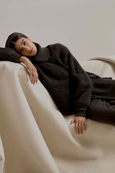 a woman laying on top of a bed covered in a white blanket and black pants