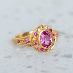 A fine grade pink sapphire has been set into our Roman Ring and is surrounded by shades of smaller pink and yellow sapphires. Centre sapphire measures 7 x 5mm and weighs 0.90ct approx. Band width 2.4mm at the back. Metal weight 6g approx. Pictured here with a matte finish. For a high shine finish please leave a note at checkout.