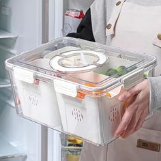 a person holding a plastic container with food in it's left hand while standing next to an open refrigerator