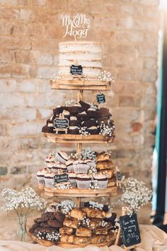 a three tiered cake and cupcake display on a table in front of a brick wall