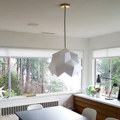 a dining room table with white chairs and an unusual light fixture hanging from the ceiling