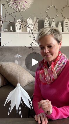 a woman sitting on top of a couch next to a white paper bird hanging from the ceiling